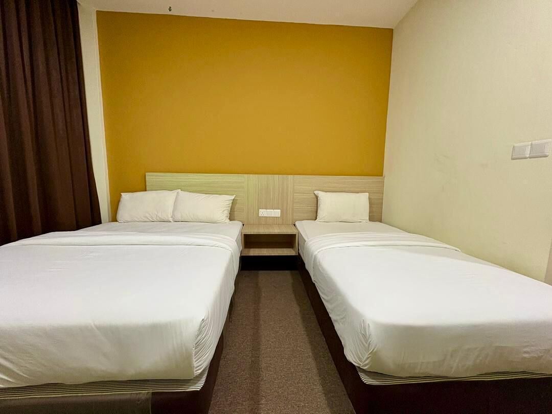 A hotel room with two single beds, a wooden headboard, a brown curtain, and a yellow accent wall.