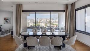 Un'area pranzo moderna con un tavolo grande e sedie, ampie finestre con tende e vista sulla città.
