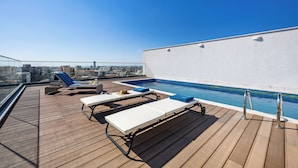 Area piscina sul tetto con poltroncine relax e vista sulla città.