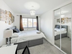A bedroom with a bed, bedside table, lamp, and a large mirror.