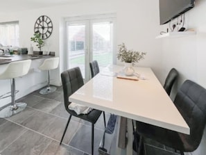A modern dining area with a white table, black chairs, and a clock on the wall.