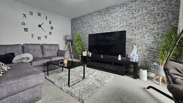Ein modernes Wohnzimmer mit grauem Sofa, Couchtisch, Flachbildfernseher, Steinwand und Lampe.