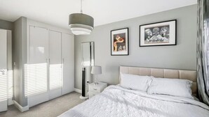 Ein Schlafzimmer mit einem großen Bett, einem Kleiderschrank, einem Nachttisch mit Lampe und gerahmten Bildern an der Wand.