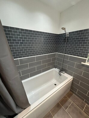 A bathroom with a white bathtub, dark tiled walls, and a shower area.