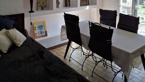 Ein Zimmer mit Esstisch, Stühlen, einer Couch und einer Wand mit Regalen, die gerahmte Bilder und Dekorationsobjekte beherbergen.