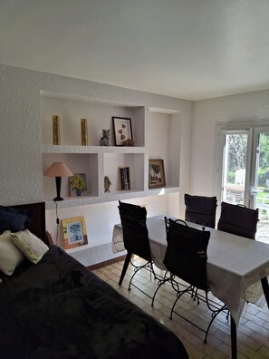 Ein Zimmer mit Esstisch, Stühlen, einer Couch und einer Wand mit Regalen, die gerahmte Bilder und Dekorationsobjekte beherbergen.