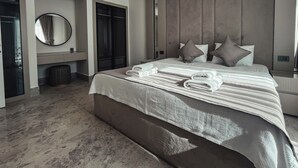 A modern hotel room with a large bed, a round mirror, a vanity with a sink, and a large window.