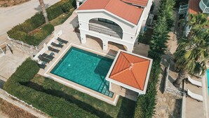An aerial view of a large house with a swimming pool, a covered patio, and a well-maintained garden.
