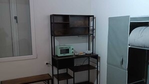 Ein Zimmer mit Holzbalkendecke, einem Fenster, einem Schreibtisch mit Toaster, einer Bank und einem Kleiderschrank.