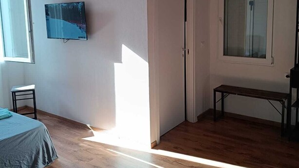 Ein Zimmer mit Holzboden, einem Bett, einem an der Wand befestigten Fernseher, einer Sitzbank und einer Tür.