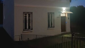 Ein zweistöckiges Gebäude mit weißer Fassade, einem Metallzaun und einer beleuchteten Außenlaterne.