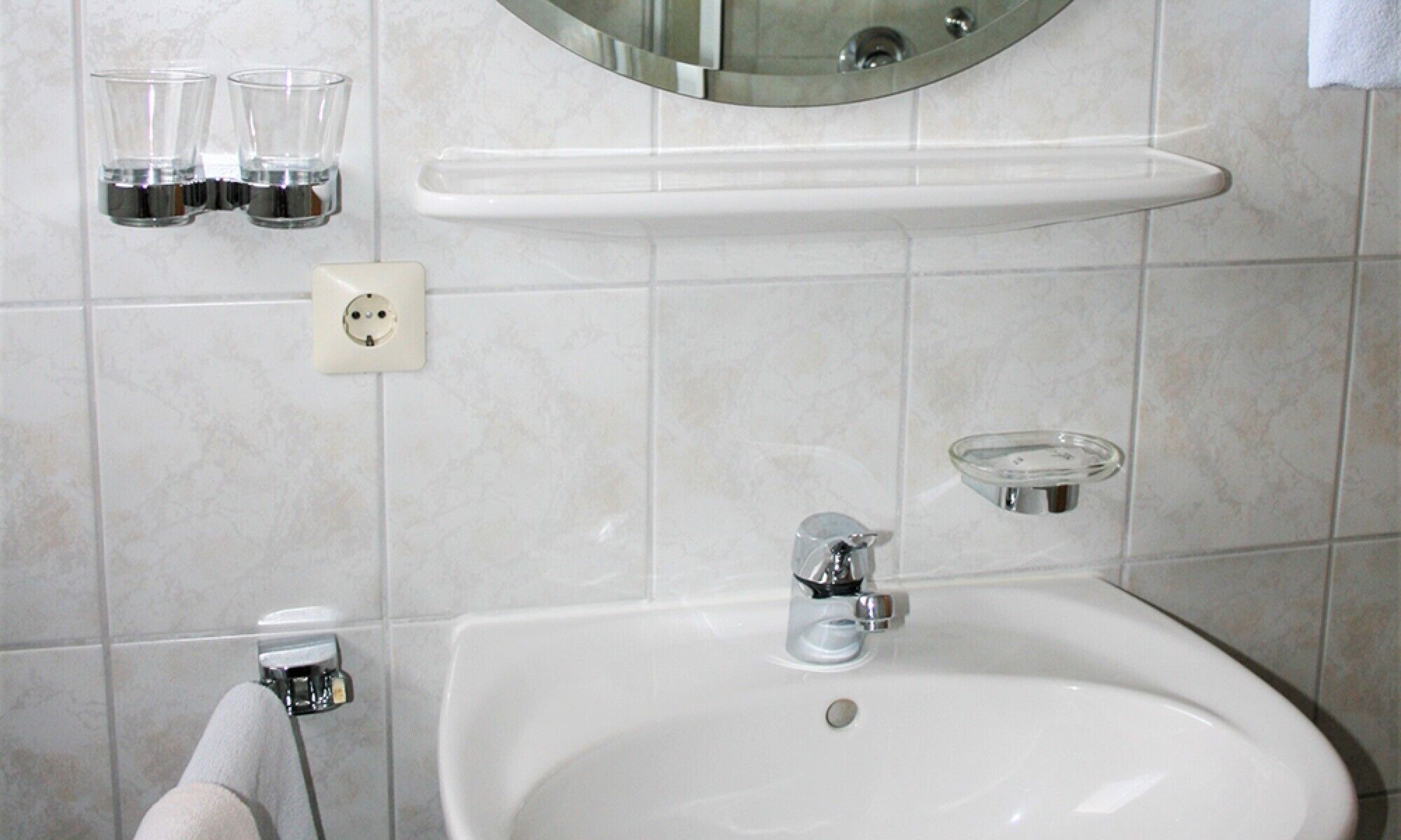 A bathroom with a sink, mirror, and two glasses on a shelf.