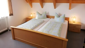 Ein Doppelbett mit Holz-Kopfteil, zwei Nachttische mit Lampen und ein Fenster mit Vorhängen.
