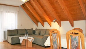 Ein Loft-Zimmer mit Holzbalkendecke, einer Couch, einem kleinen Tisch mit Wasserflaschen und einem Sessel.