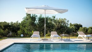 A poolside area with a white umbrella, two lounge chairs, and a small table. - Exclusive, Modern Country House with Private Pool – Your Dream Holiday in Puglia (Puglia)