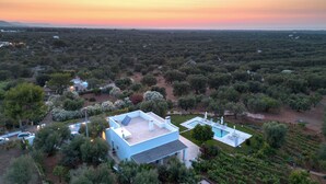 A modern house with a large patio and a swimming pool, surrounded by dense vegetation and a sunset sky. - Exclusive, Modern Country House with Private Pool – Your Dream Holiday in Puglia (Puglia)