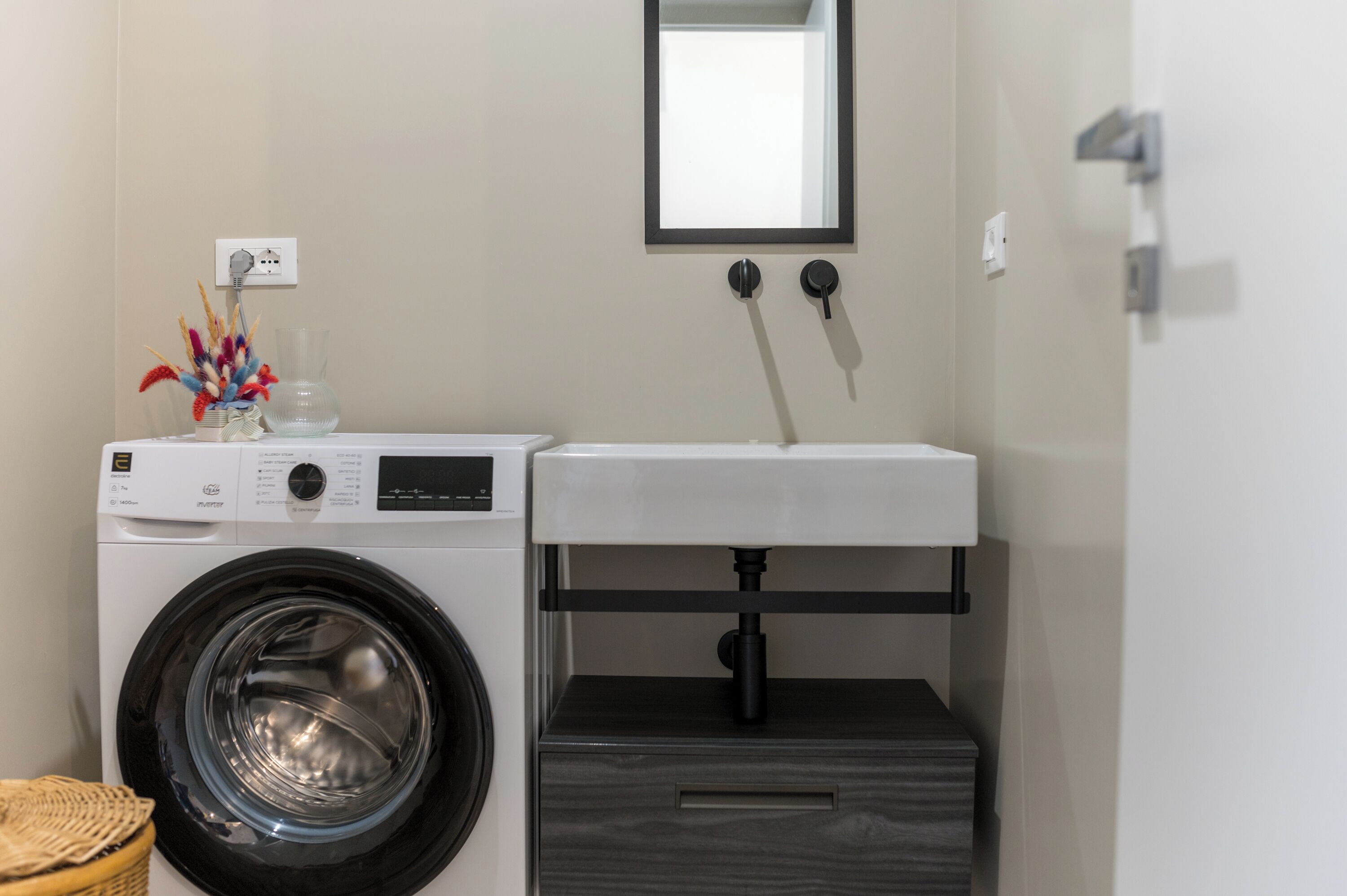 A compact laundry area with a front-loading washing machine, a sink, and a small cabinet.