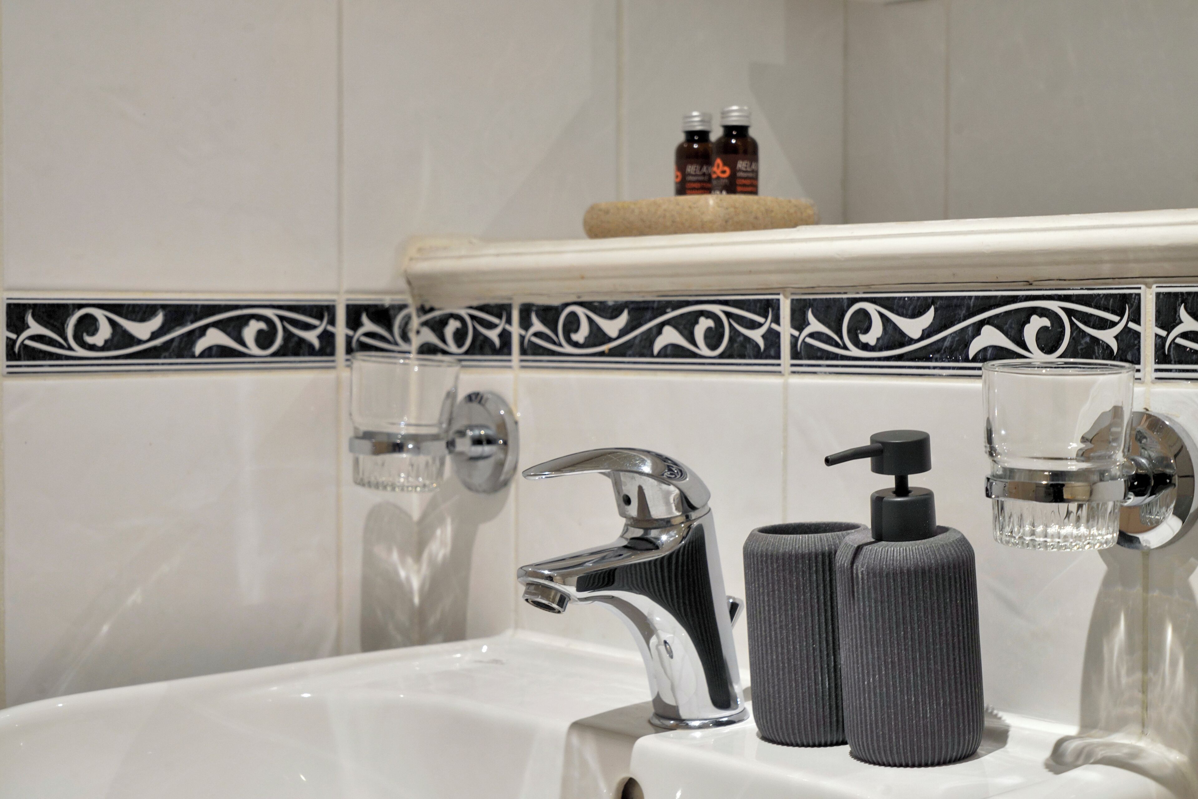 A bathroom with a white sink, chrome faucet, and a soap dispenser. There are two bottles on the shelf above the sink.