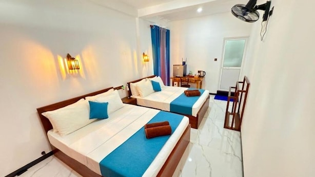 A hotel room with two beds, a desk, a chair, and a TV. - Devon Surf . Inn : Deluxe Family Room (Dikwella)