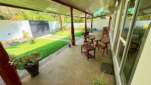 A covered patio area with a concrete floor, wooden furniture, and potted plants. - Devon Surf . Inn : Deluxe Family Room (Dikwella)