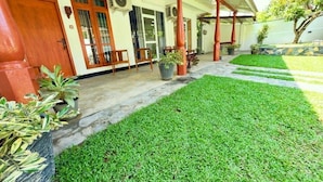A well-maintained front porch with a stone pathway leading to the entrance, surrounded by potted plants and a neatly trimmed lawn. - Devon Surf Inn : Standard Double Room (Dikwella)