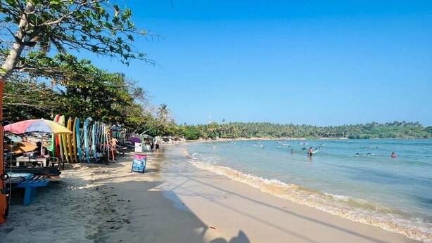 A beach with surfboards, umbrellas, and beachgoers. - Devon Surf Inn : Standard Double Room (Dikwella)