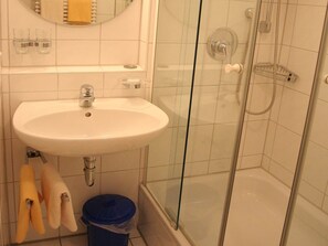 Et badeværelse med en hvid vask, et brusebad med glasvægge og en blå skraldespand.