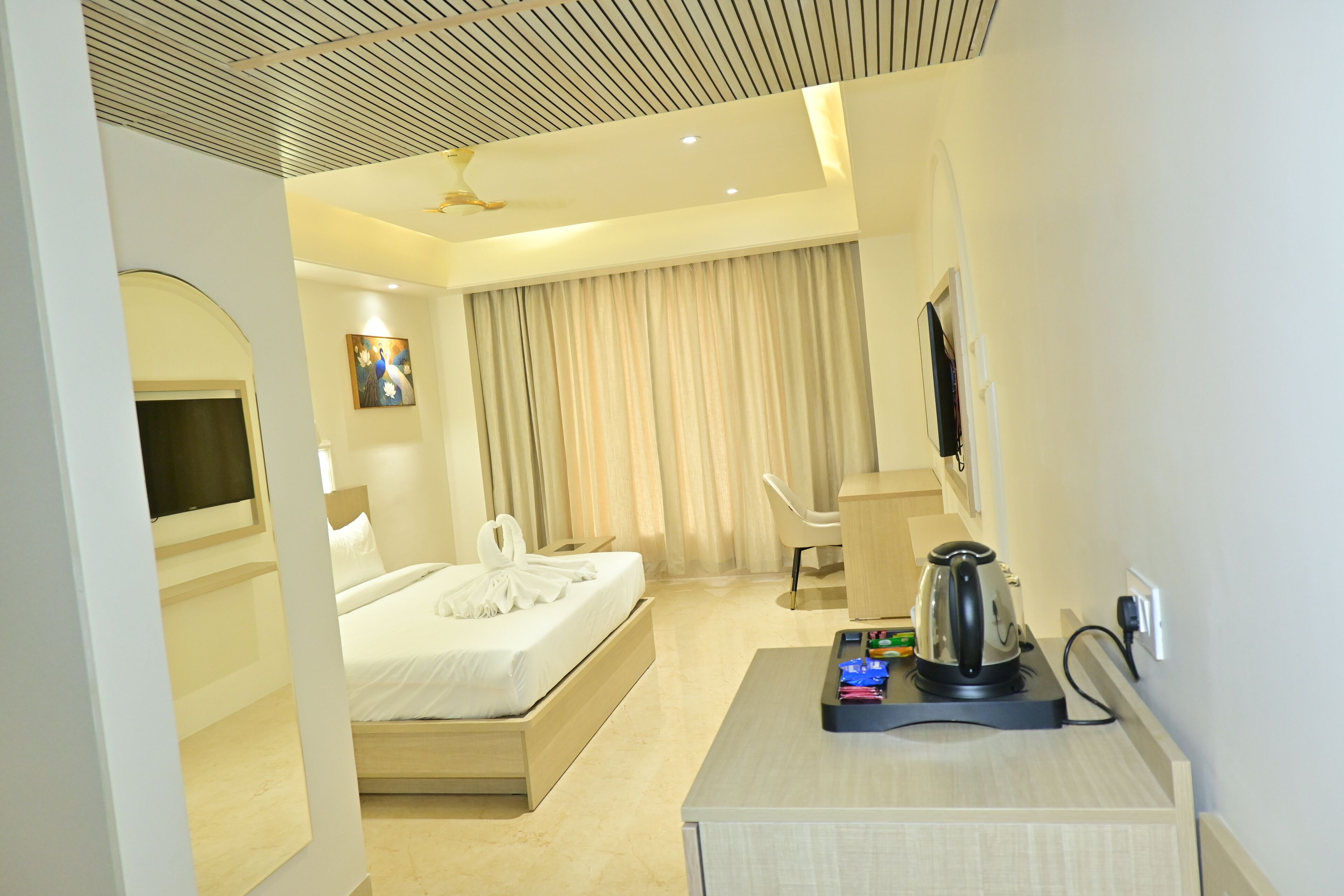 A hotel room with a bed, a desk with a kettle, a chair, and a television.
