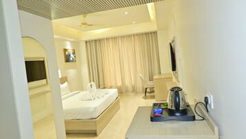 A hotel room with a bed, a desk with a kettle, a chair, and a television.