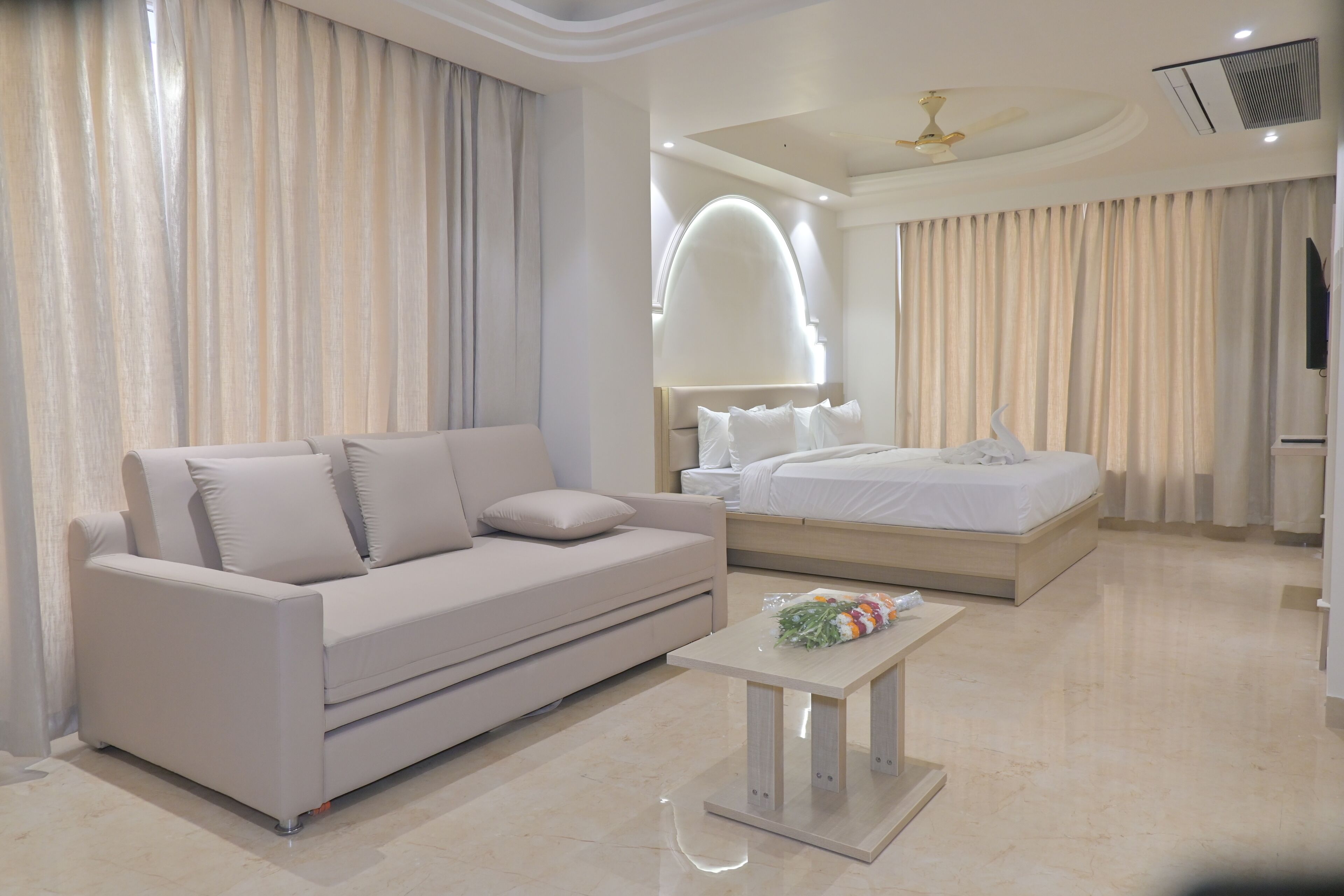 A modern hotel room with a sofa, a bed, a small table, and a ceiling fan.
