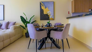 A modern dining area with a table set for four, surrounded by chairs, a potted plant, and a painting on the wall. - Bloomfields 1BR Canal The View Raha (Abu Dhabi)