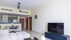 A modern living room with a white sofa, a black coffee table, and a TV on a black stand. - Bloomfields 1BR Canal The View Raha (Abu Dhabi)