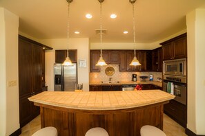 Une cuisine dotée d’un îlot central, de meubles en bois foncé, d’appareils électroménagers en acier inoxydable et de luminaires suspendus.