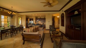 A spacious living room with a large sofa, a dining area with a table and chairs, a kitchen in the background, and a television on the right. - Marbella 1E 3 bdr Ocean View in Los Suenos (Jacó)