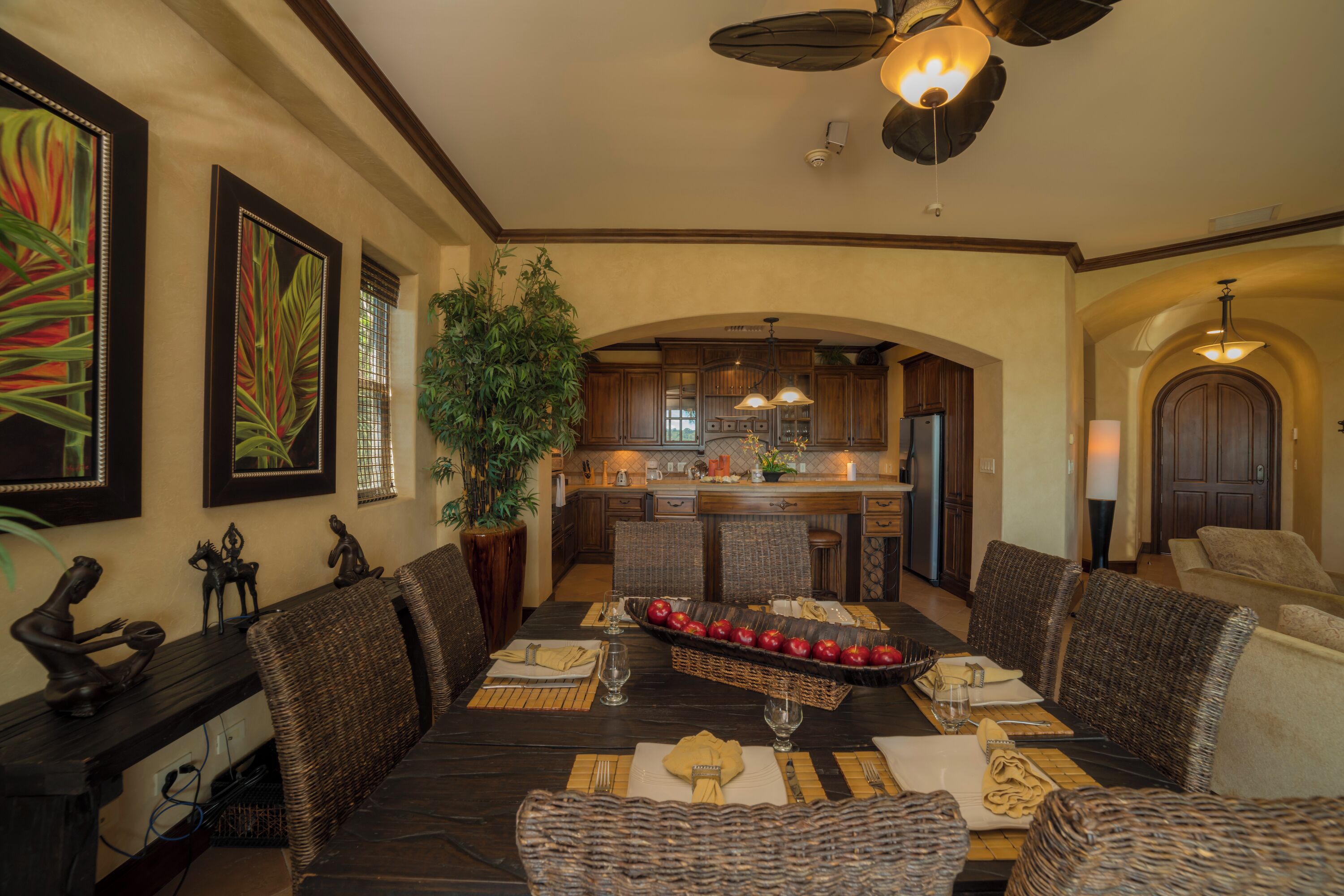 A dining area with a dark wooden table, wicker chairs, and a central fruit display.