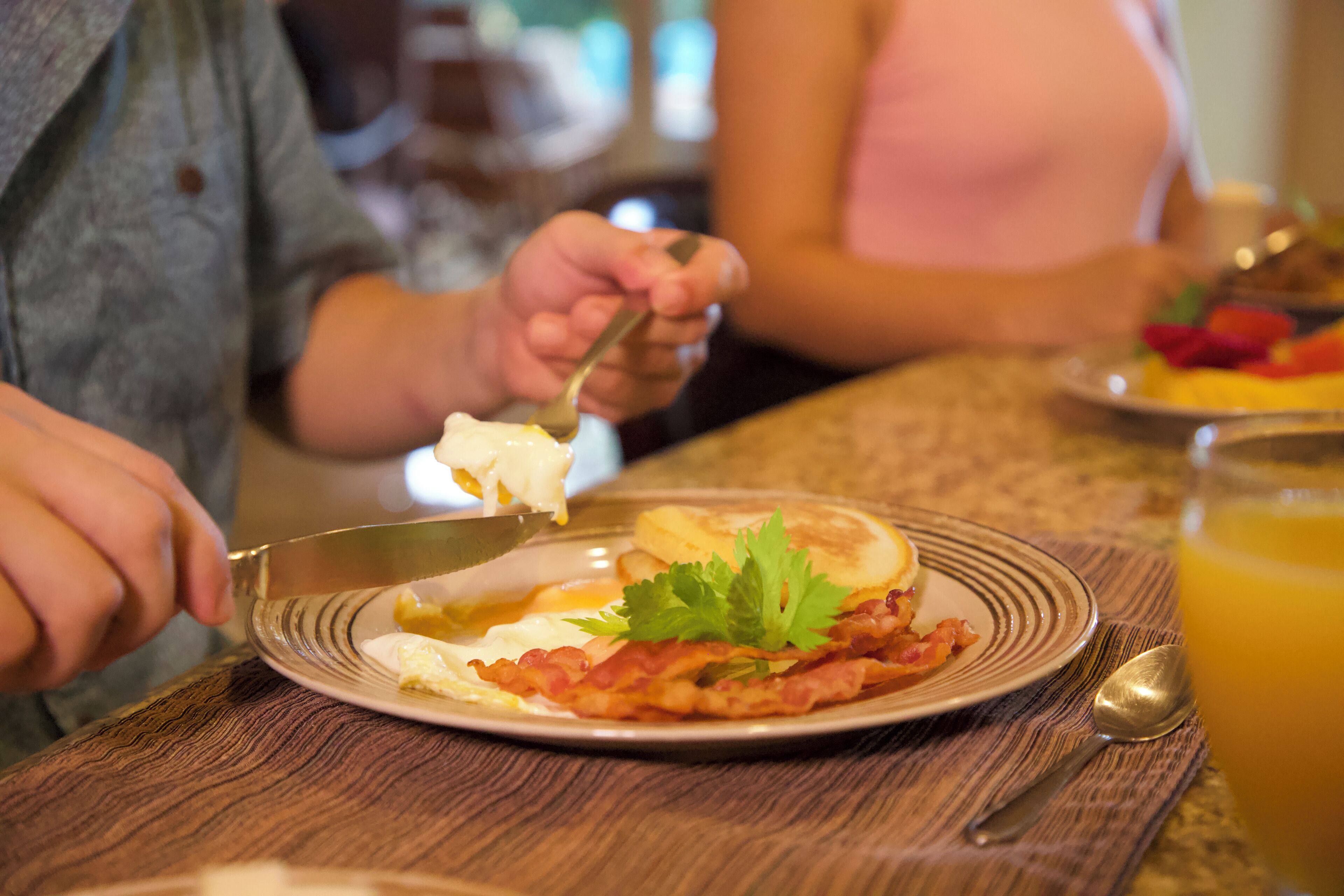 Una colazione servita su un tavolo di legno: uova, pancetta, pane tostato, un cucchiaio e un bicchiere di succo d'arancia.