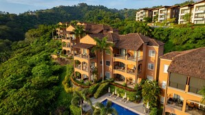 A multi-story hotel with balconies, a swimming pool, and lush greenery. - Altavista 4C 3 bdr Ocean View in Los Suenos (Jacó)