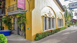 Facciata di un hotel con rivestimento giallo, un balcone con ringhiera in ferro battuto e una insegna pubblicitaria che offre servizi come banco informazioni turistiche e affitti vacanze.