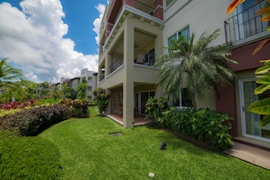 Un immeuble résidentiel à plusieurs étages, doté de balcons, d’une pelouse bien entretenue et de plantes tropicales.