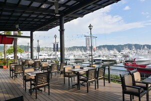 Un área de estar al aire libre con mesas y sillas, con vistas a un puerto deportivo con numerosos barcos.