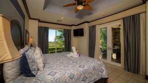 Ein geräumiges Schlafzimmer mit einem großen Bett, einem Deckenventilator, einem Fernseher und Blick ins Freie durch eine Glastür.