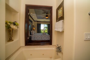 A bathroom with a large bathtub, a ceiling fan, and a view of a bedroom with a bed and window. - Vista Bahia 3F 1 bdr Ocean View in Los Suenos (Jacó)