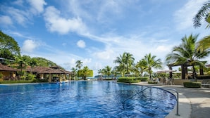 A large outdoor swimming pool with a clear blue sky, surrounded by palm trees and lounge chairs. - Del Mar 5J 3 bdr Garden View in Los Suenos (Jacó)