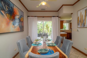 A dining area with a long wooden table set for six, surrounded by six grey upholstered chairs. - Veranda 4C 3 bdr Golf Course View in Los Suenos (Jacó)