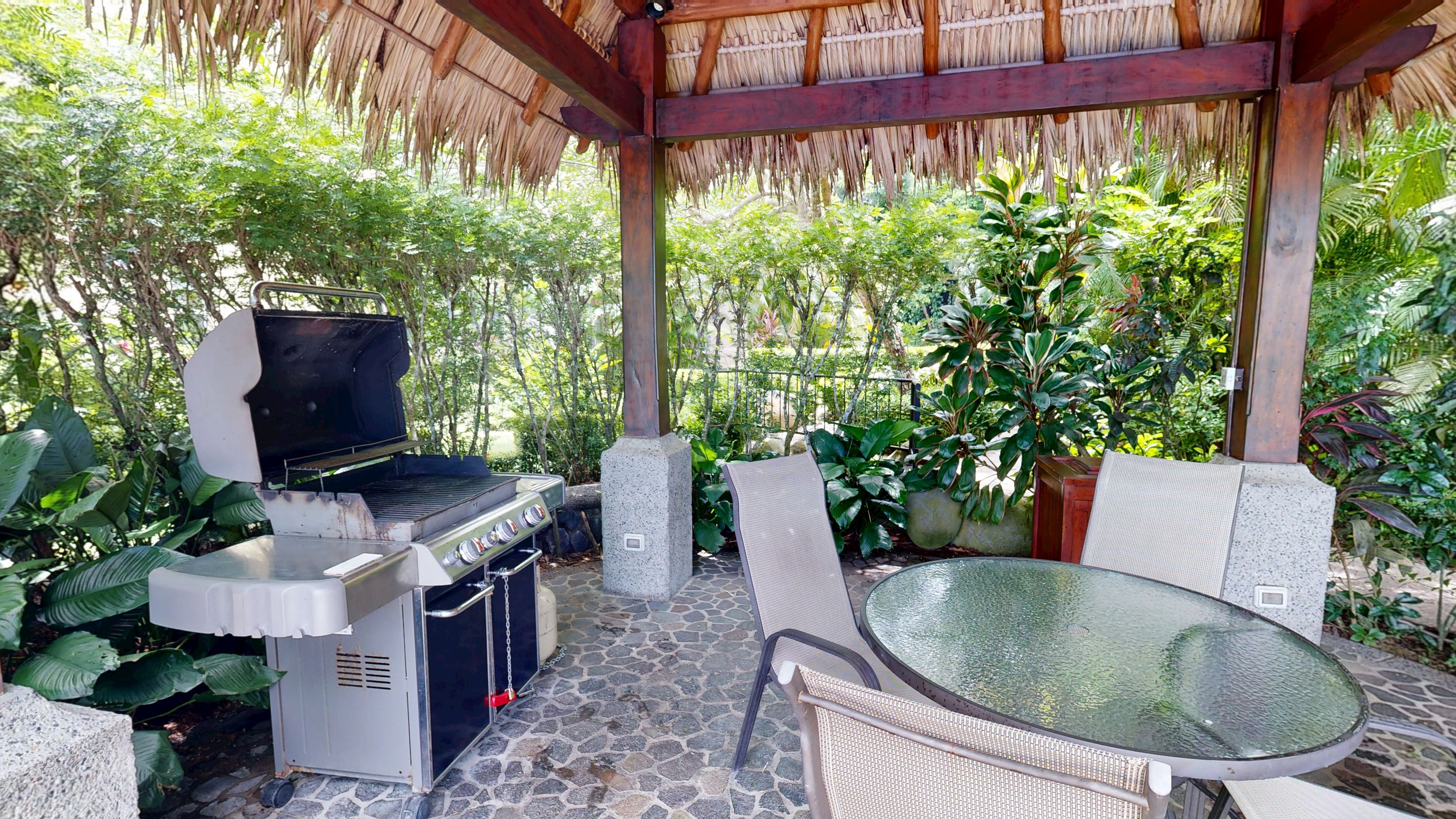 An outdoor patio with a grill, seating, and a thatched roof structure.