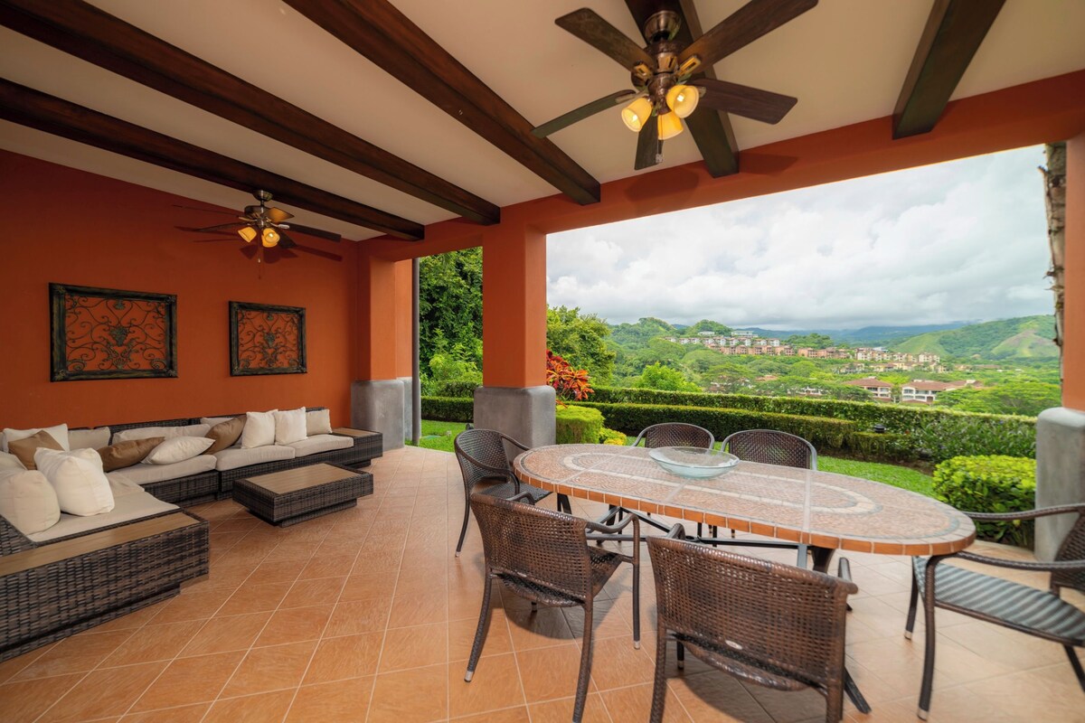 A covered patio with a dining table and chairs, a sofa, and two ceiling fans.