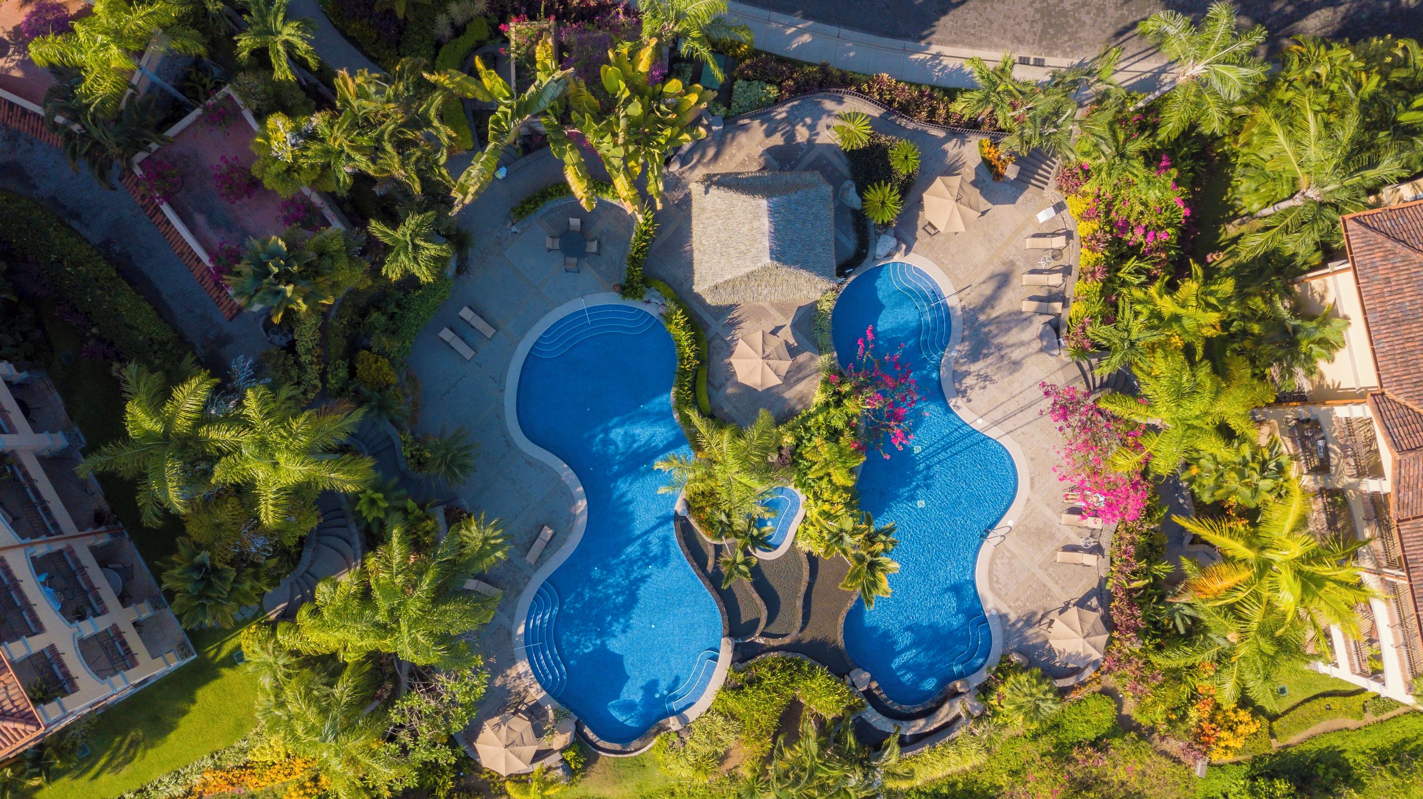 An aerial view of a resort with multiple swimming pools, palm trees, and lounge areas.