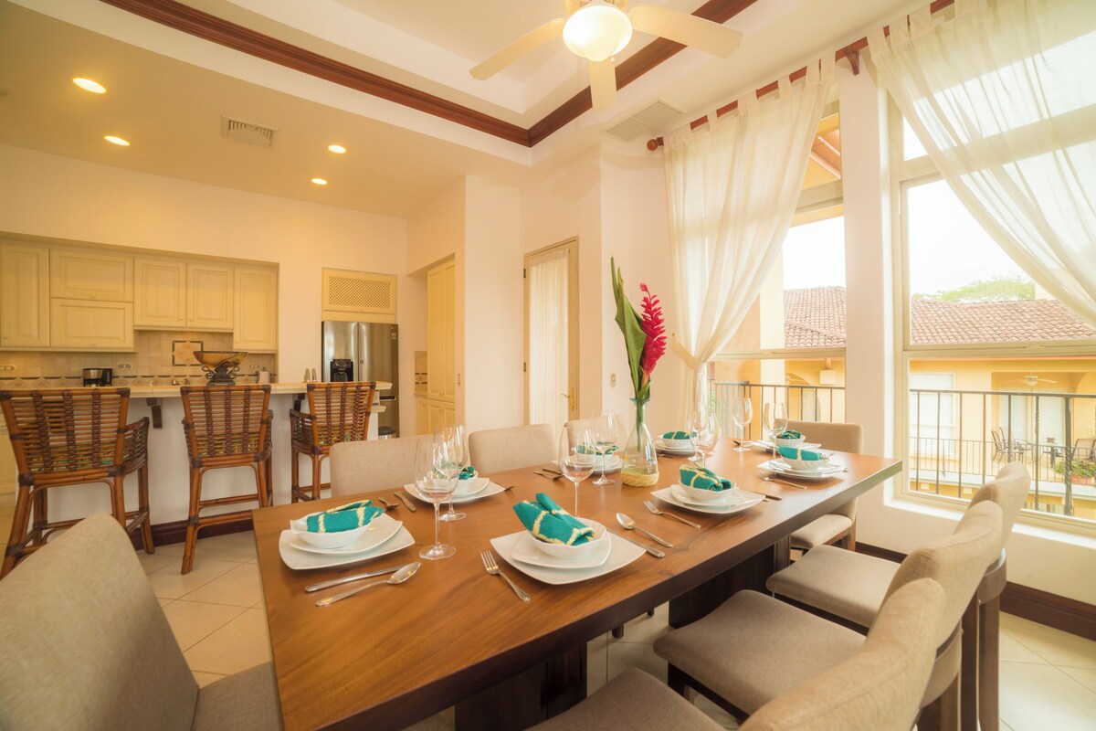 A dining area with a wooden table set for four, surrounded by wicker chairs.