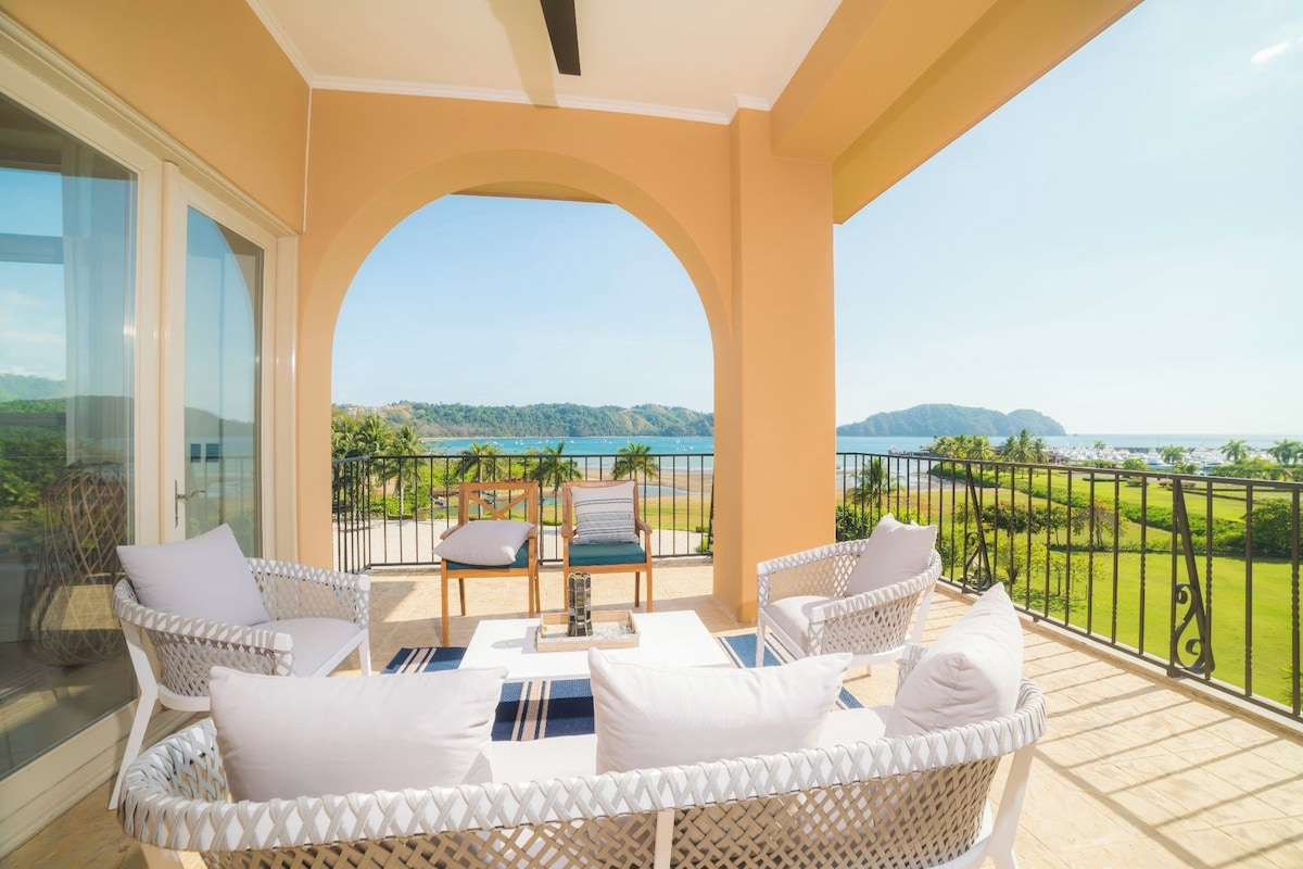 A balcony with wicker furniture, a view of the sea, and a clear sky.