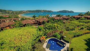 A resort with a pool surrounded by lush greenery, overlooking a beach and the sea.